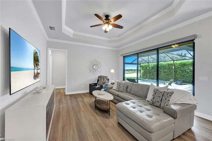 Living area with light wood-type flooring, a tray ceiling, a ceiling fan, crown molding, and a sunroom