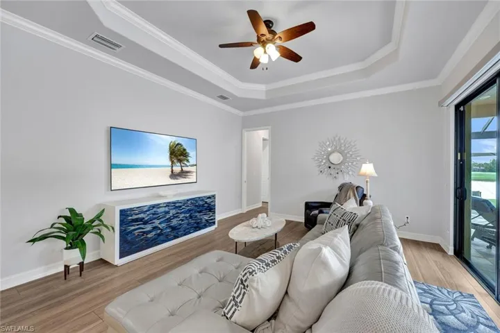 Living room featuring a tray ceiling, ornamental molding, light wood-style flooring, and ceiling fan