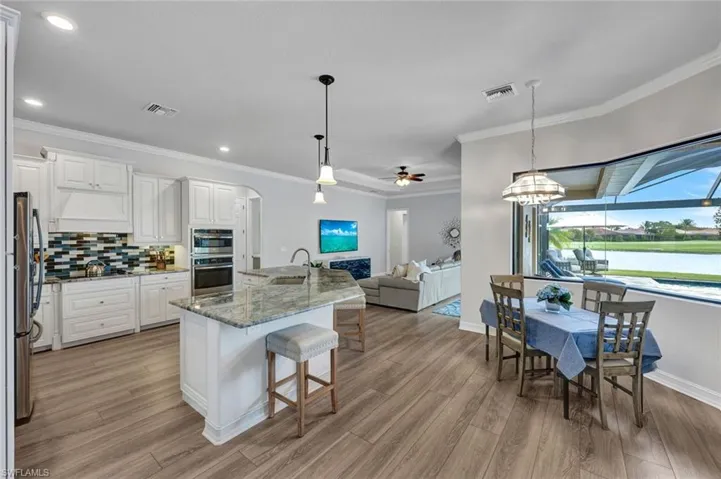 Kitchen featuring arched walkways, decorative light fixtures, a kitchen bar, light stone countertops, and a kitchen island with sink