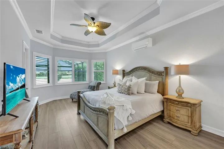Bedroom featuring a tray ceiling, ornamental molding, a ceiling fan, light wood-type flooring, and a wall mounted air conditioner