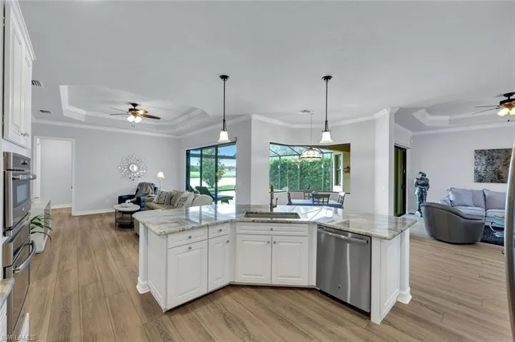 Kitchen featuring ceiling fan, open floor plan, a tray ceiling, white cabinets, and ornamental molding
