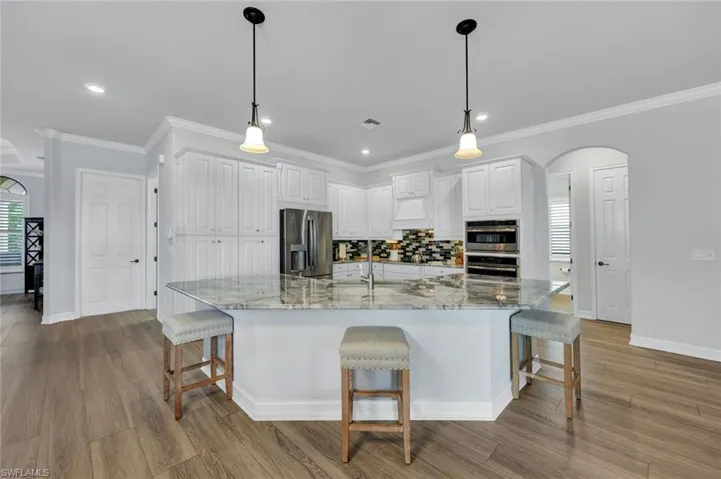 Kitchen featuring a kitchen bar, white cabinets, arched walkways, a large island with sink, and ornamental molding