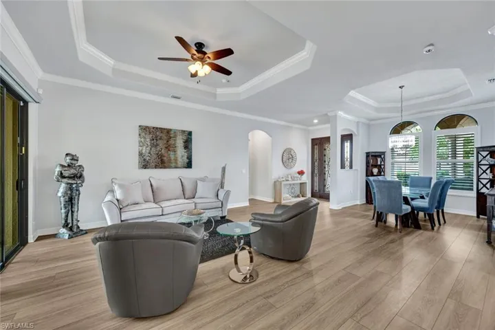 Living room featuring a tray ceiling, crown molding, light wood-style floors, ceiling fan, and arched walkways