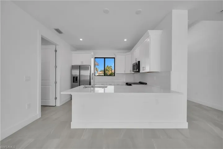 Kitchen with white cabinetry, a peninsula, light stone countertops, stainless steel microwave, and recessed lighting