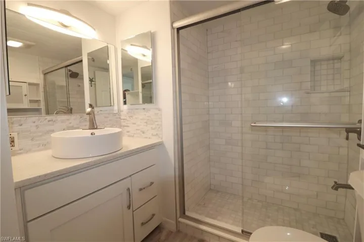 Bathroom with backsplash, vanity, and a shower stall