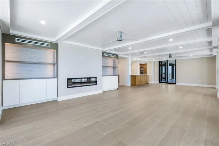 Lving room featuring recessed lighting, light wood-type flooring, a ceiling fan, a glass covered fireplace, and a wooden ceiling with exposed beams