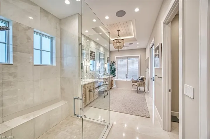 Bathroom featuring a freestanding tub, vanity, a tray ceiling, recessed lighting, and a tile shower