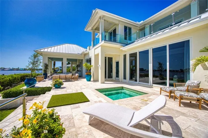 Back of property featuring an in-ground hot tub, a patio, a balcony, a standing seam roof, and stucco siding
