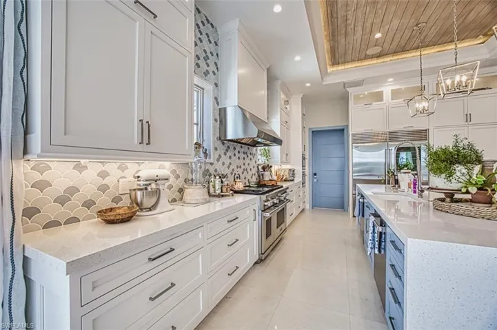 Kitchen featuring high quality appliances, a raised ceiling, wall chimney range hood, decorative backsplash, and white cabinets