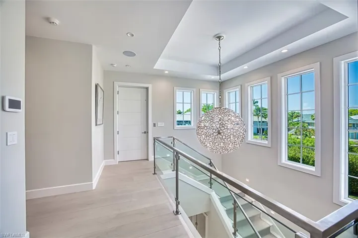 Corridor with light wood-style flooring, a raised ceiling, an upstairs landing, recessed lighting, and a chandelier