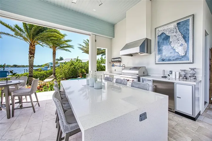 Kitchen with wall chimney exhaust hood, white cabinetry, a kitchen breakfast bar, a kitchen island, and a towering ceiling