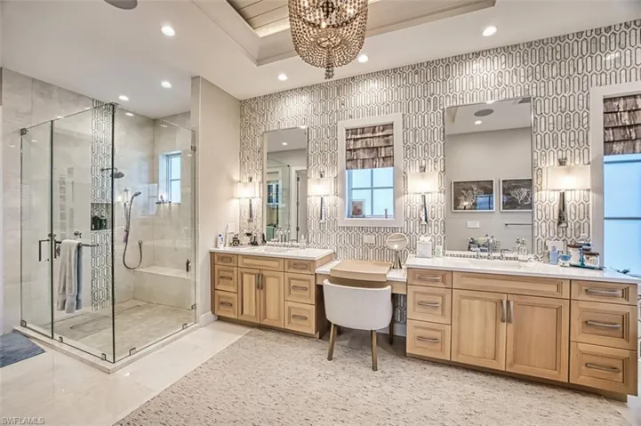 Bathroom featuring a shower stall, a chandelier, two vanities, recessed lighting, and a raised ceiling