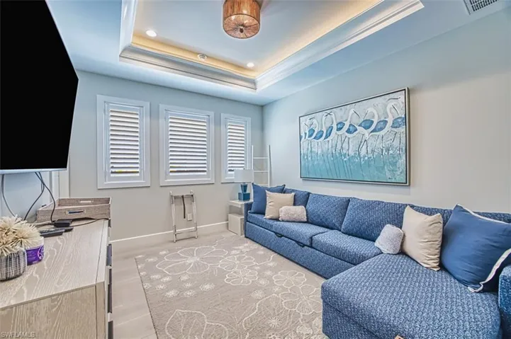 Living area featuring a raised ceiling, light wood-style flooring, recessed lighting, and ornamental molding