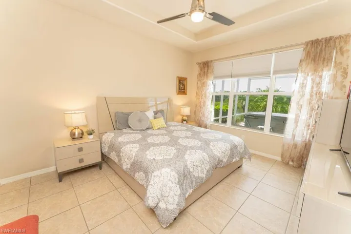 Bedroom featuring light tile patterned flooring, baseboards, a tray ceiling, and a ceiling fan