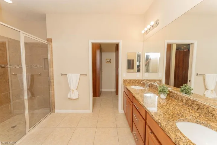Bathroom with double vanity, tile patterned floors, a shower stall, and baseboards