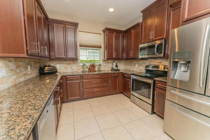 Kitchen featuring stainless steel appliances, tasteful backsplash, dark stone counters, light tile patterned flooring, and recessed lighting