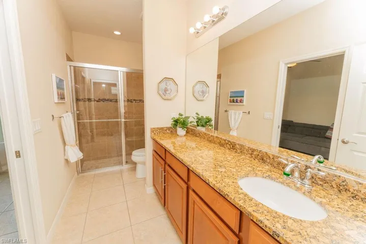 Ensuite bathroom featuring tile patterned flooring, a shower stall, vanity, toilet, and baseboards