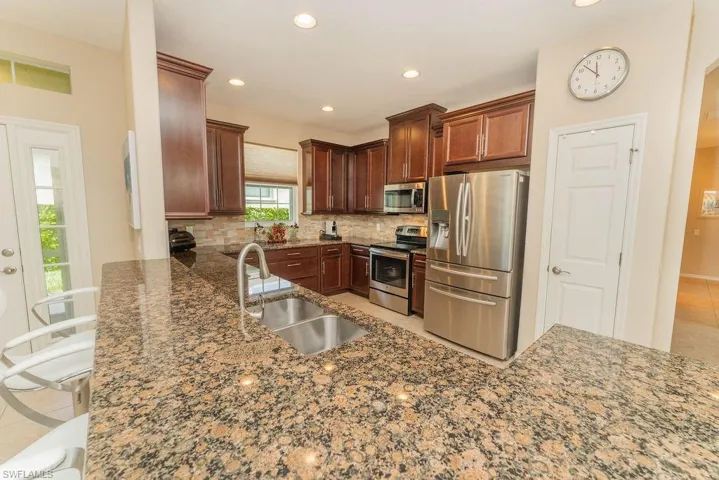 Kitchen with stainless steel appliances, a sink, backsplash, dark stone countertops, and recessed lighting