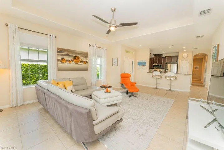 Living room featuring arched walkways, light tile patterned flooring, a raised ceiling, ceiling fan, and baseboards