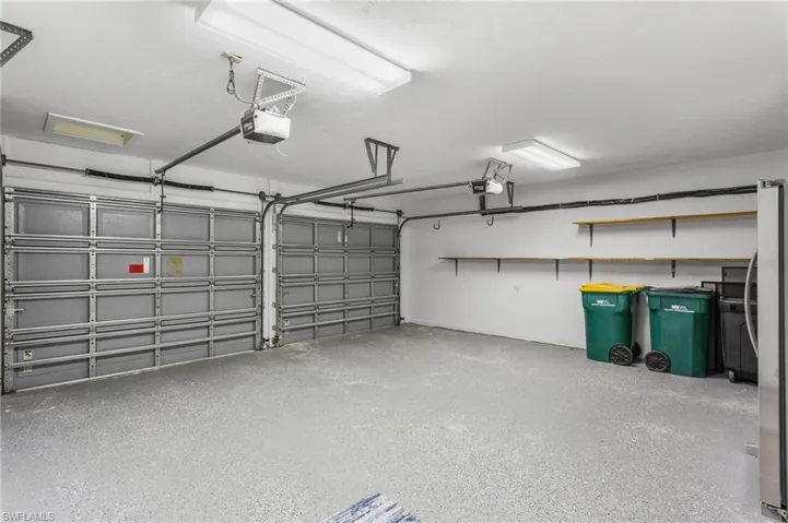 Large garage with epoxy flooring, shelves, extra cabinetry, and new refrigerator.
