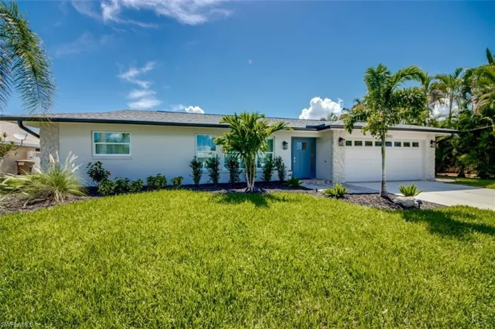 The property features a well-maintained lawn, a two-car garage, and a light-colored exterior with stone accents