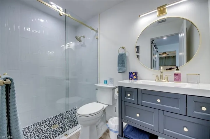 The bathroom features a glass-enclosed shower with white tiled walls and a black pebble floor