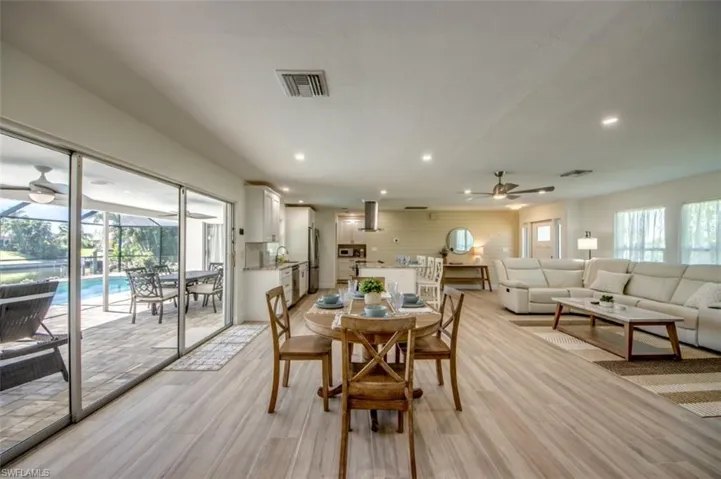 Expansive open-concept living area featuring light-toned flooring, recessed lighting, and a kitchen with white cabinetry