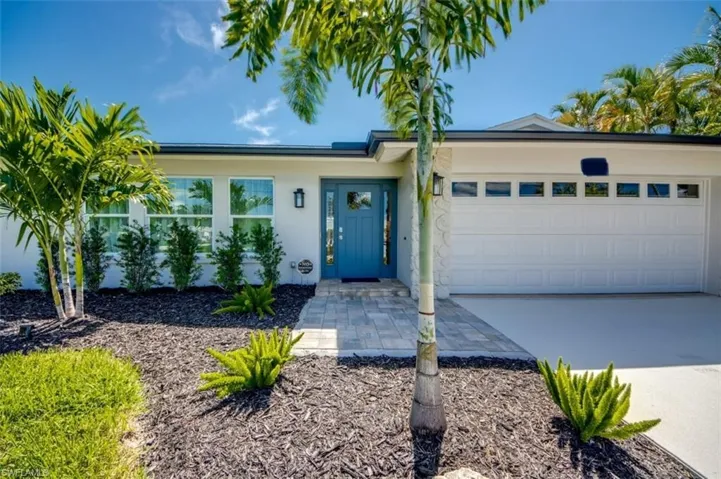 The property features a white exterior, a blue front door, and a white garage door with rectangular windows