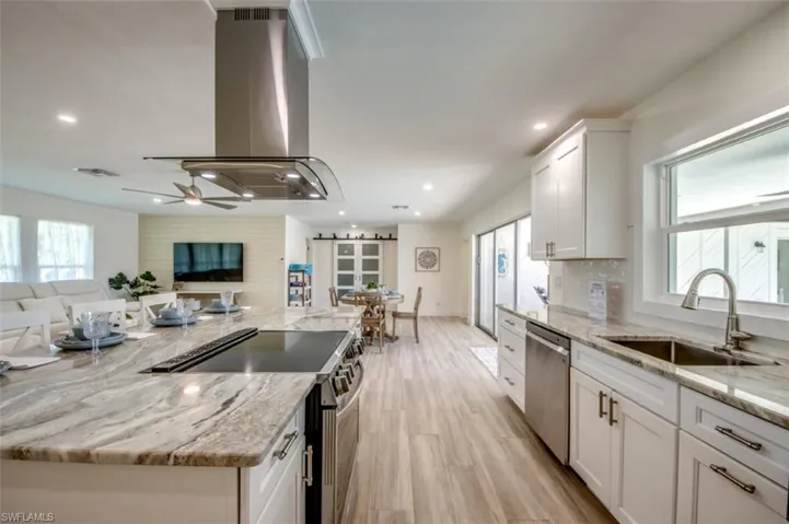The kitchen features a large island with a cooktop, granite countertops, white cabinetry, and stainless steel appliances, including a dishwasher and range hood