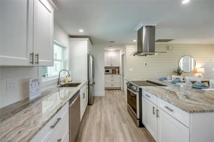 The kitchen features white cabinetry, stone countertops, stainless steel appliances, and wood-look flooring