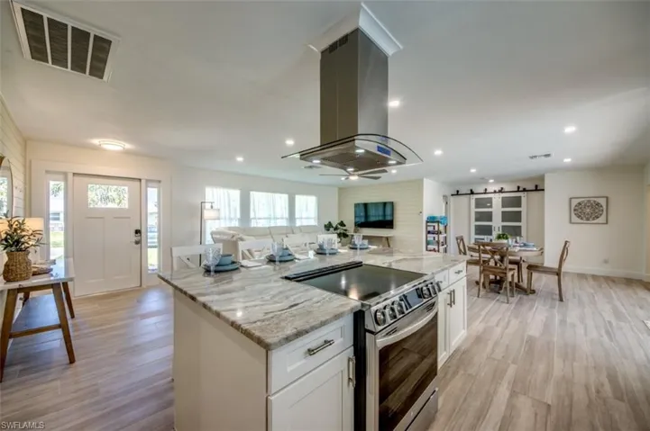 The kitchen features a central island with a built-in electric range, a stainless steel range hood, and granite countertops
