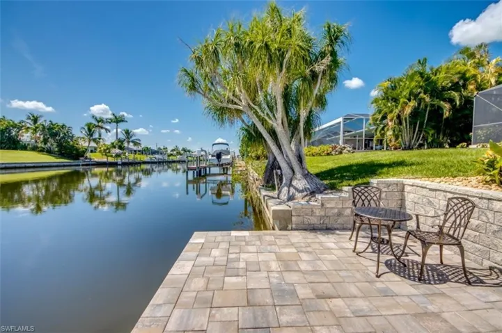 Waterfront property with a paved patio, a retaining wall, and a mature tree