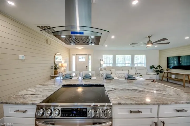 The kitchen showcases a large island with a cooktop, a stainless steel range hood, and white cabinetry