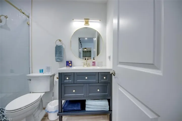 This bathroom features a contemporary vanity with a white countertop and gold-toned hardware, a circular mirror, and a white toilet