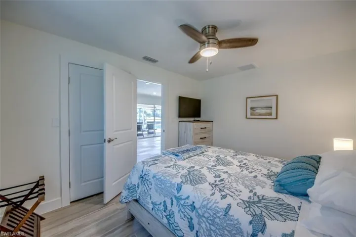 This bedroom features a ceiling fan with light, light-colored walls, and a television on a dresser