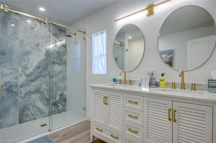 This bathroom features a double vanity with white cabinetry and gold-toned hardware, topped with a light-colored countertop, and two circular mirrors illuminated by a gold-toned light fixture
