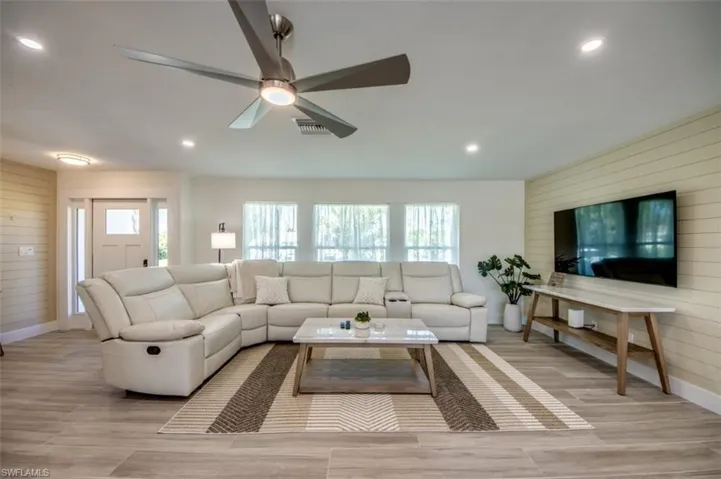 The living area features light wood-look flooring, recessed lighting, and a modern ceiling fan