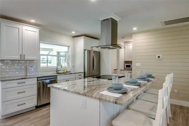Well-appointed kitchen featuring white cabinetry, stainless steel appliances, granite countertops, and a central island with seating