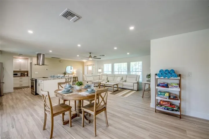 The expansive open-concept living area features light-toned flooring, recessed lighting, and a modern kitchen with a stainless steel range hood and white cabinetry