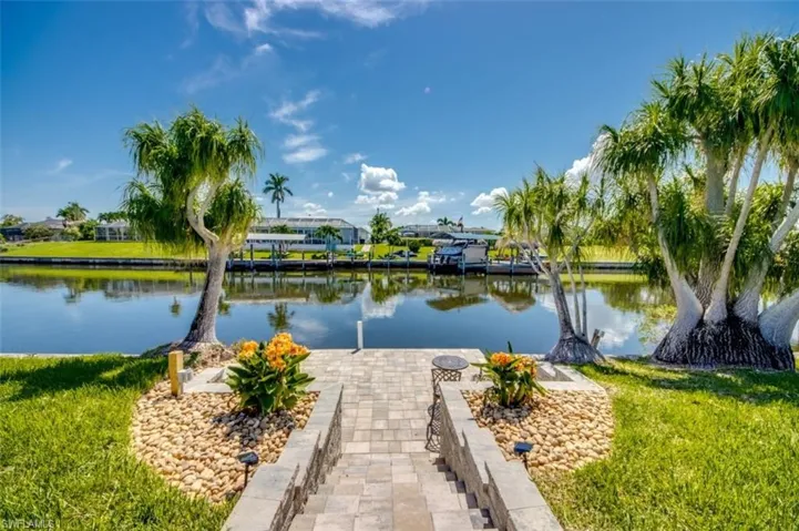 The property features a paved walkway leading to the waterfront, surrounded by landscaped areas with decorative stones and vibrant plants