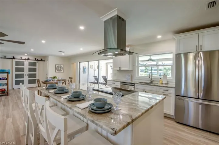 The kitchen features a large island with a granite countertop, a stainless steel refrigerator, and white cabinetry