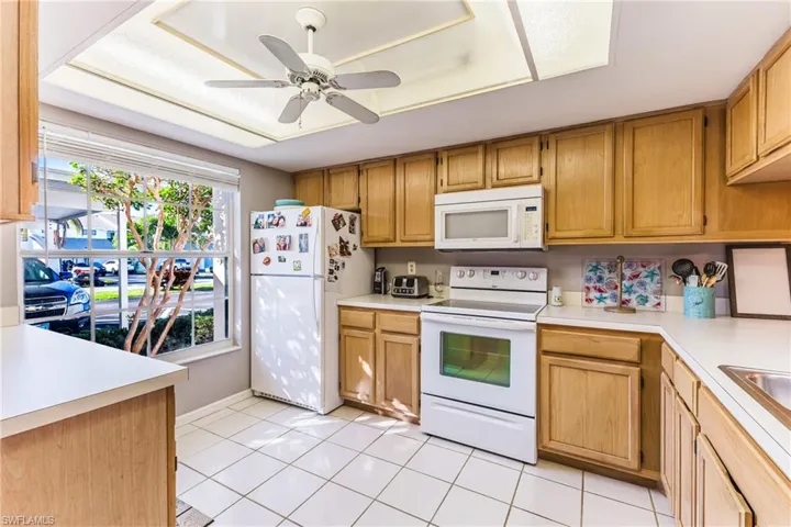 Kitchen with white appliances, light countertops, light tile patterned flooring, and ceiling fan