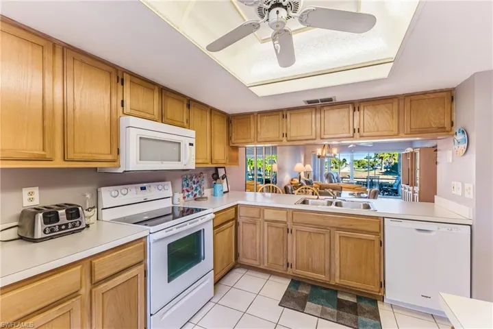 Kitchen with ceiling fan, white appliances, light countertops, light tile patterned floors, and a tray ceiling