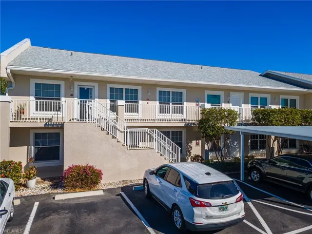 View of property with uncovered parking and stairs