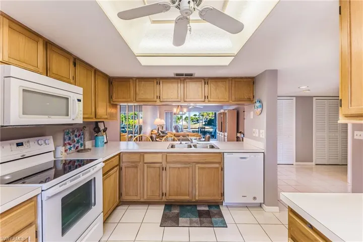 Kitchen with white appliances, a ceiling fan, light tile patterned floors, light countertops, and brown cabinets