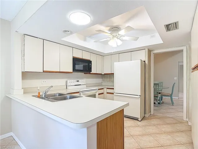 Kitchen with white appliances, a peninsula, light countertops, light tile patterned flooring, and white cabinetry