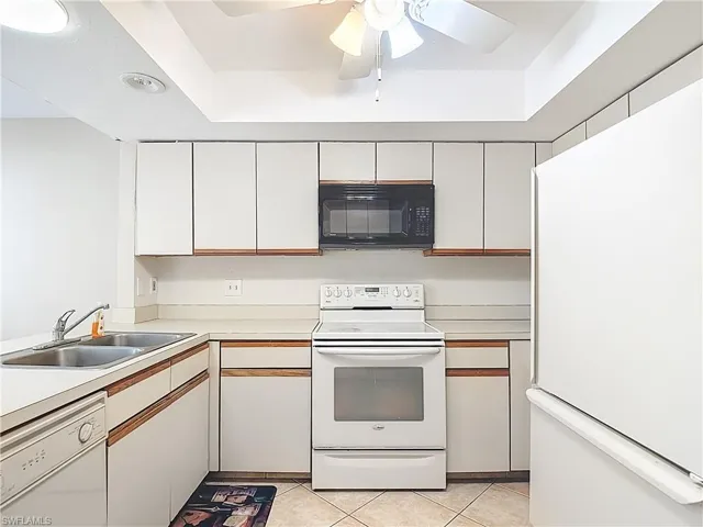 Dual tone kitchen with white appliances, two tone cabinets, light countertops, light tile patterned floors, and a ceiling fan