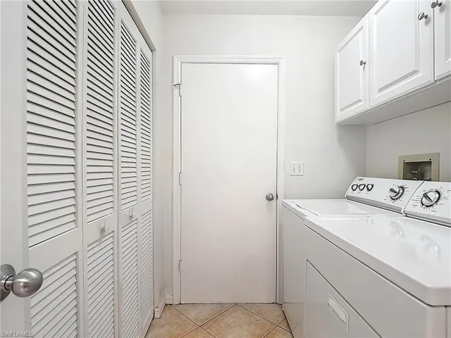 Laundry area with light tile patterned floors, cabinet space, and washer and clothes dryer