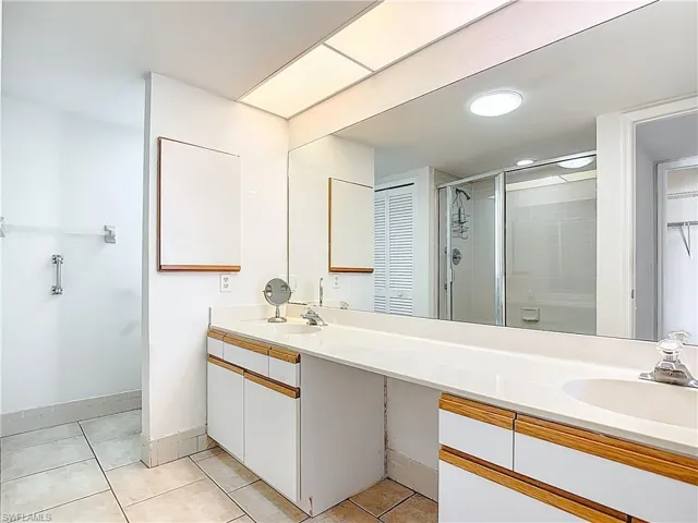 Bathroom featuring a shower stall, double vanity, light tile patterned flooring, and a spacious closet
