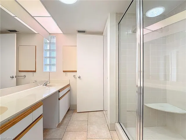 Bathroom with a shower stall, double vanity, and light tile patterned floors